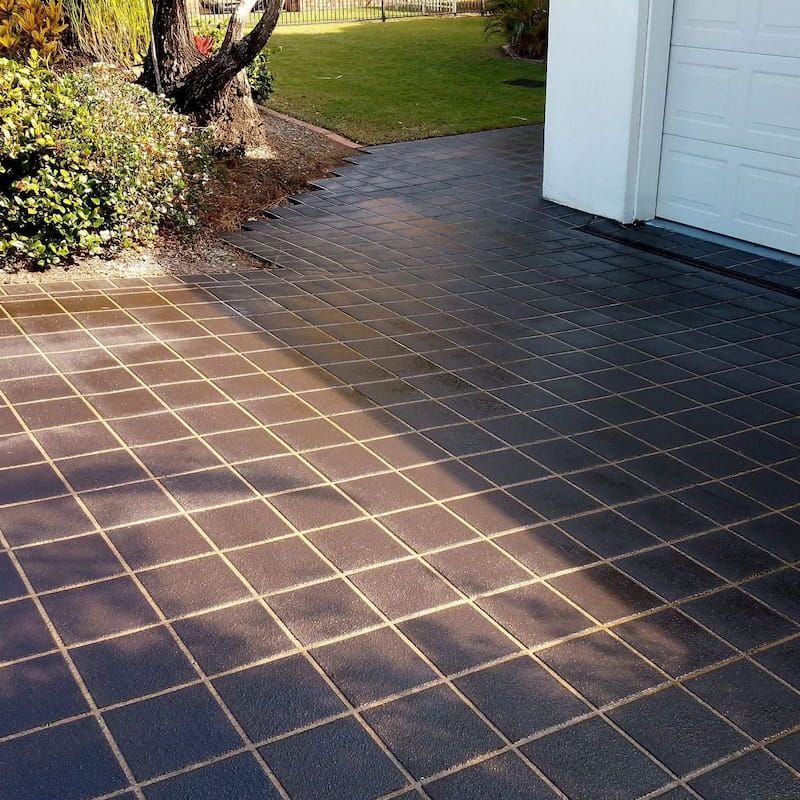 Dark tiled patio beside a white garage, with sunlight and trees casting shadows across the ground. — Troys Concrete Overlays in Hillcrest, QLD
