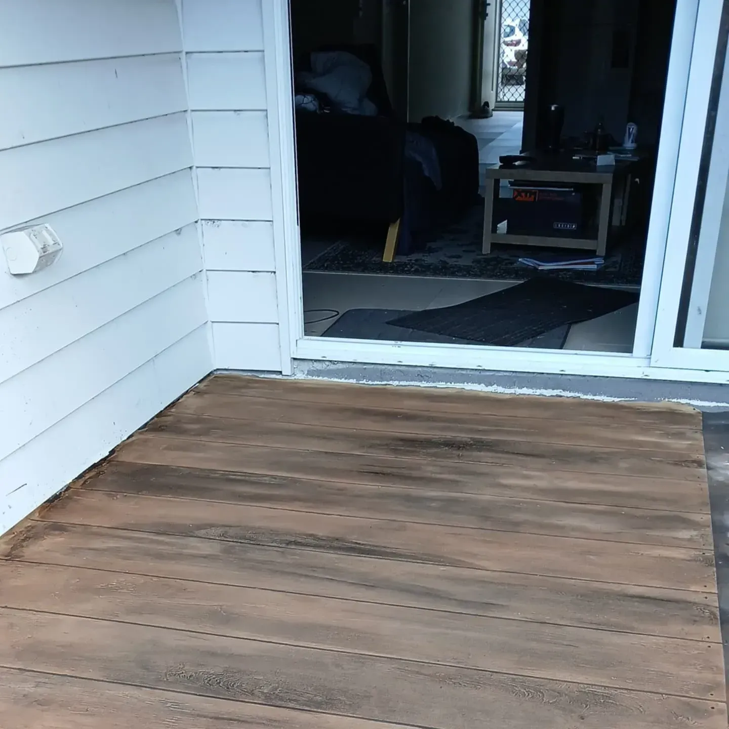 A Wooden Deck With a Sliding Glass Door in the Background — Troys Concrete Overlays in Hillcrest, QLD