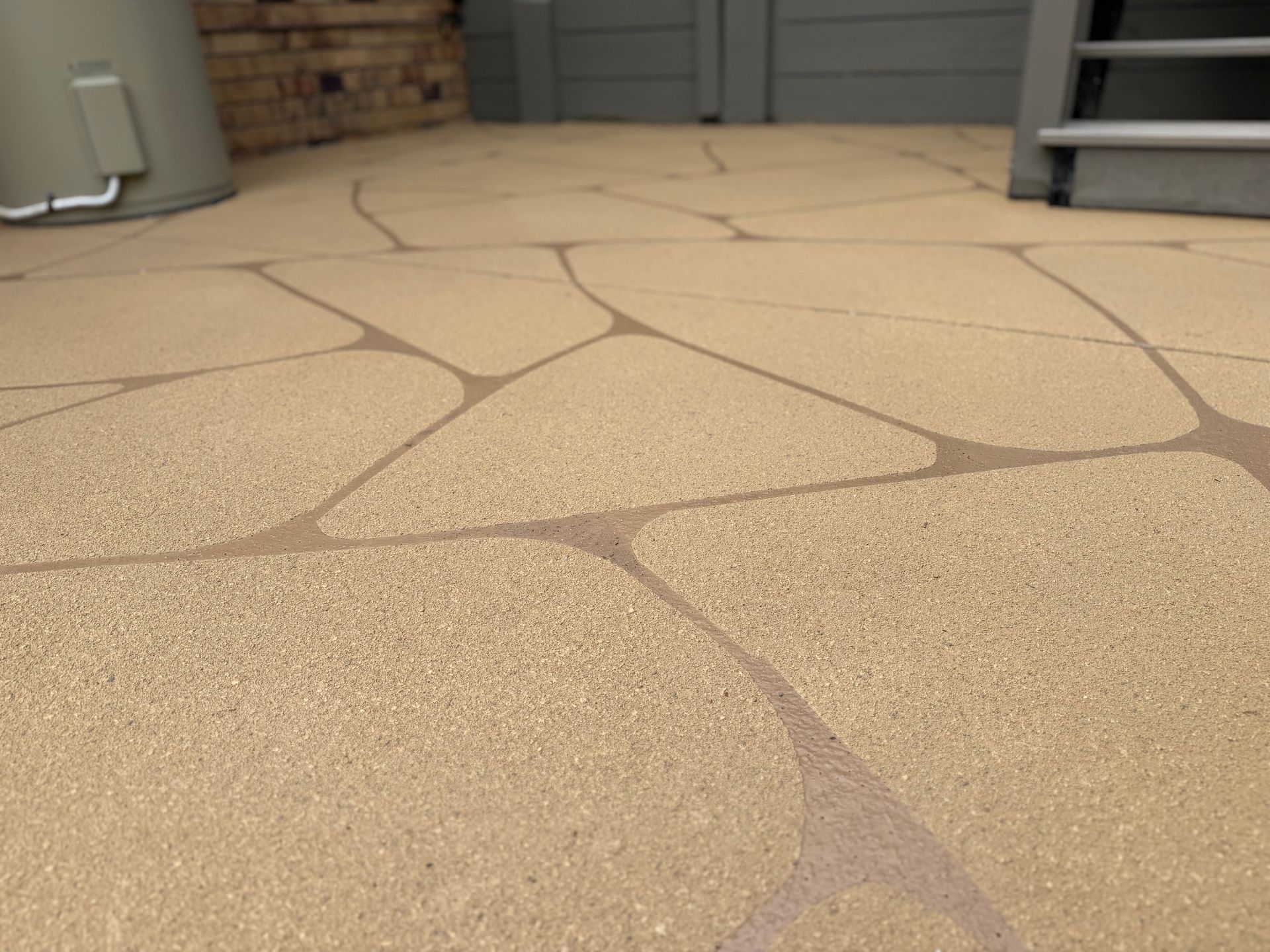 Textured tan concrete patio with irregular stamped stone pattern near a garage doorway — Troys Concrete Overlays in Hillcrest, QLD