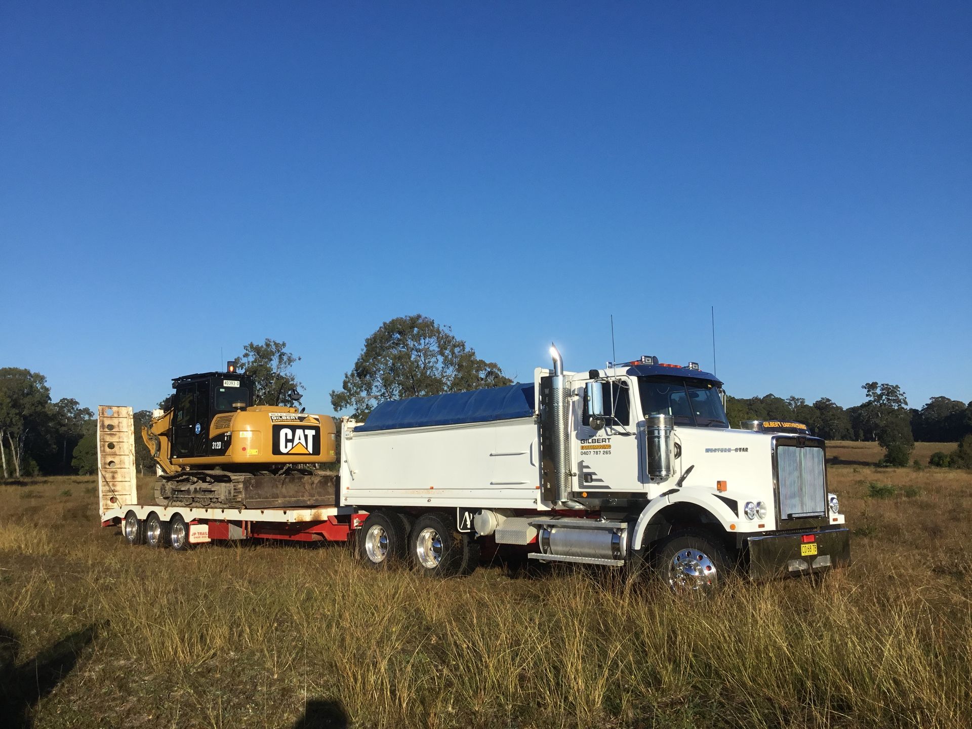 A White Truck is Carrying a Cat Excavator on a Trailer — S M & A J Gilbert Earthmoving in Mitchells Island, NSW