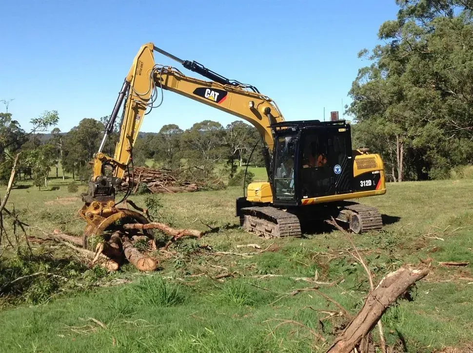 A Yellow Cat Excavator is Working in a Grassy Field — S M & A J Gilbert Earthmoving in Mitchells Island, NSW