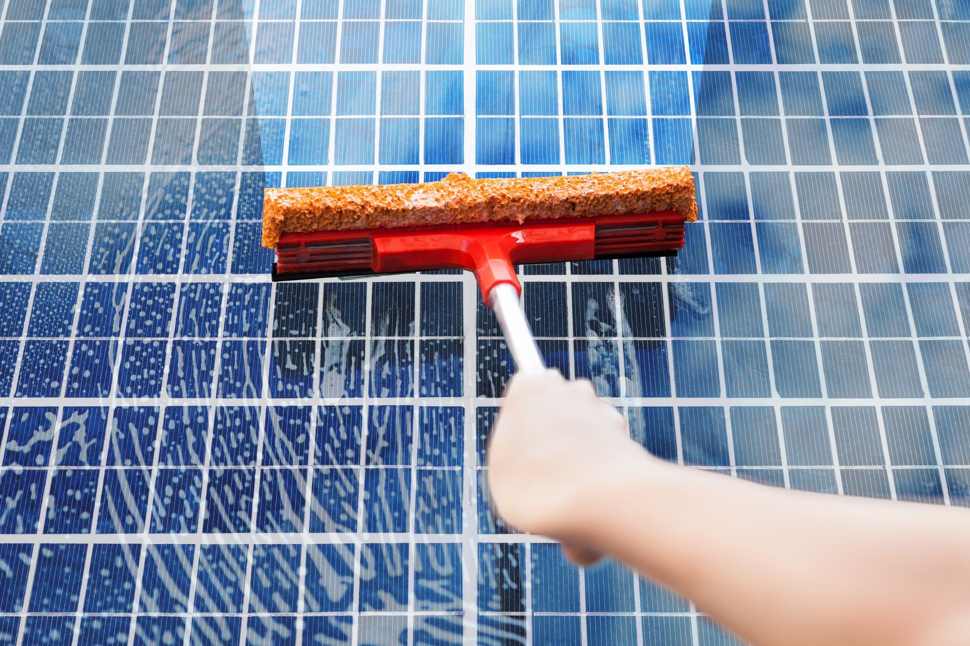 Person cleaning a blue solar panel with a red squeegee on a white pole