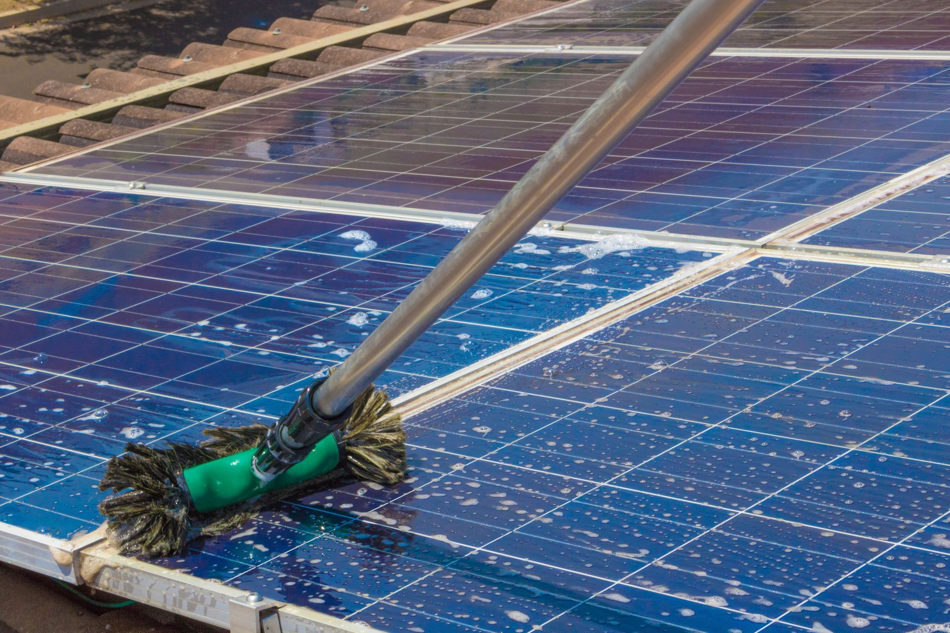 A squeegee cleans blue solar panels on a rooftop.