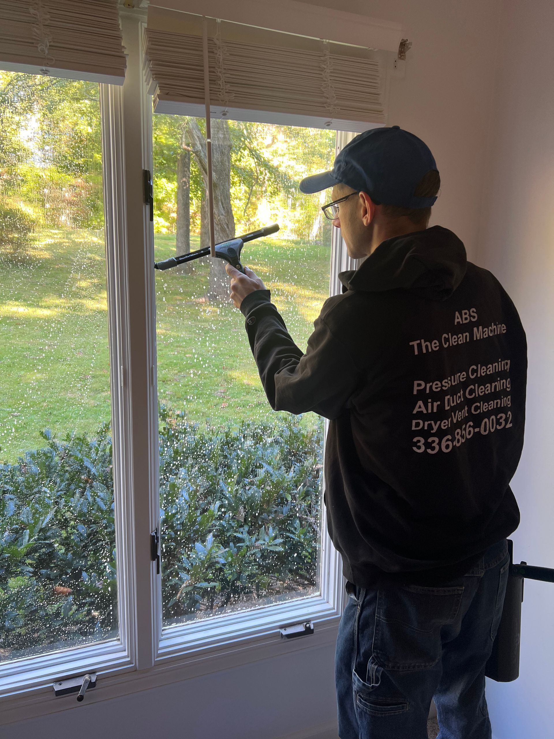 Worker cleaning a window with a long-handled tool in a sunlit room