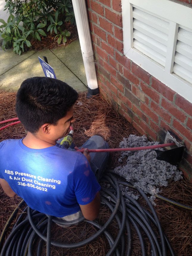 Person using a hose to spray water on a brick wall and ground beside a house.