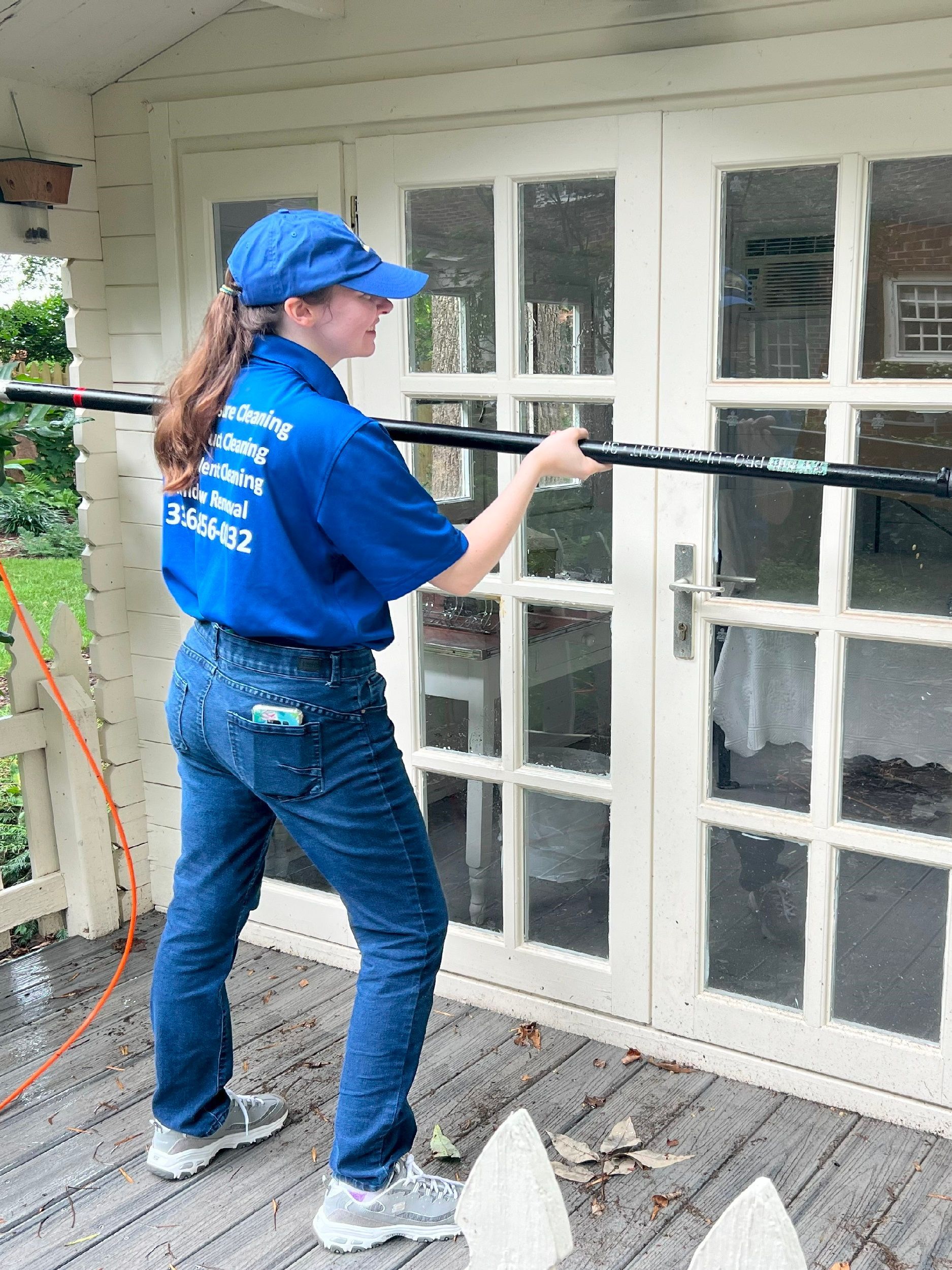 Person in blue shirt and cap cleaning white French doors with a pressure washer on a porch