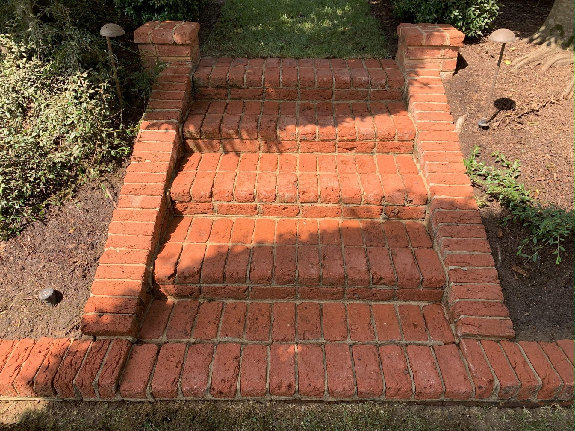 Brick garden steps with low side walls and a brick path, bordered by grass and soil.