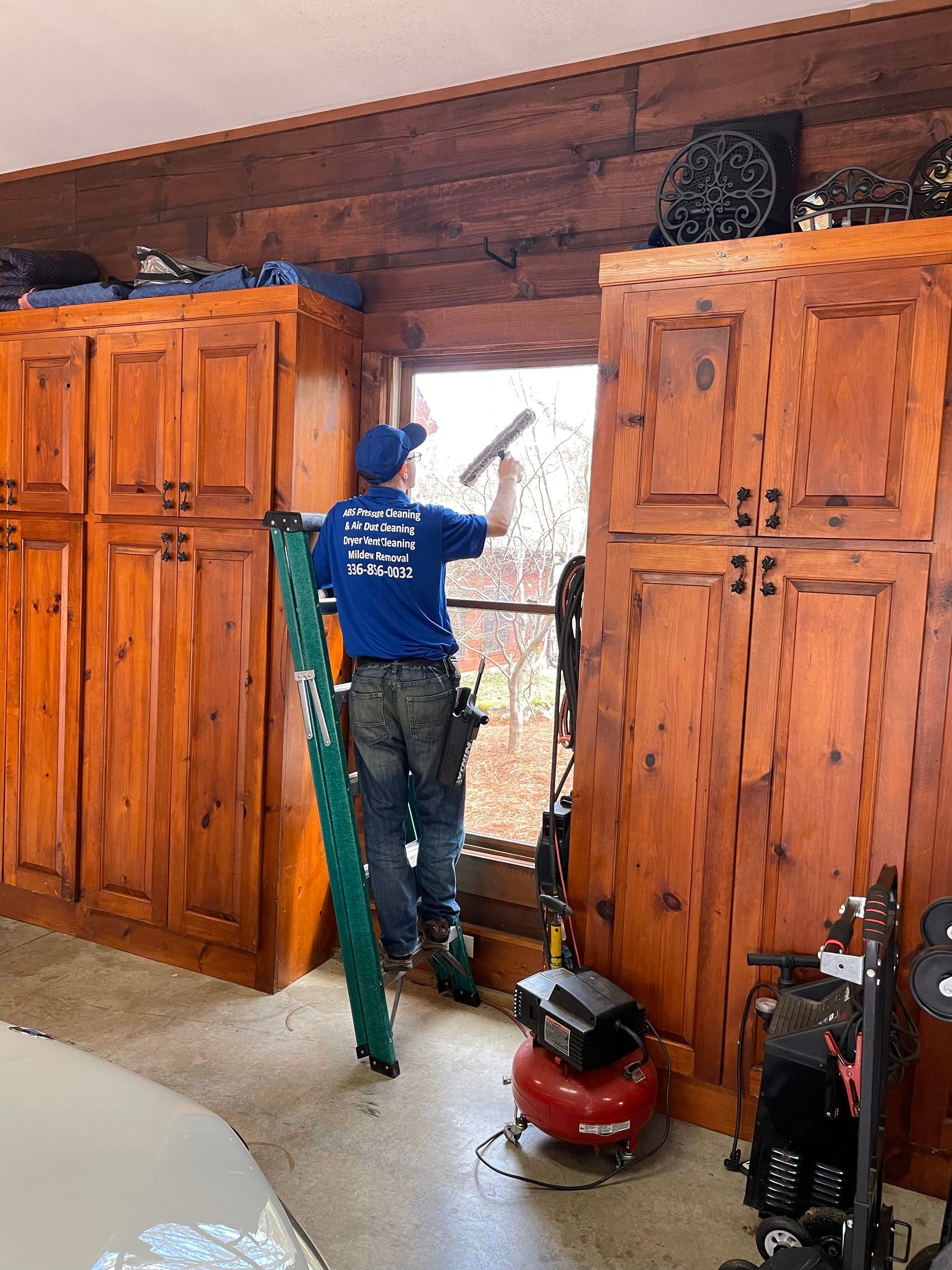 Person painting a wooden doorframe inside a garage with large wooden cabinets nearby.