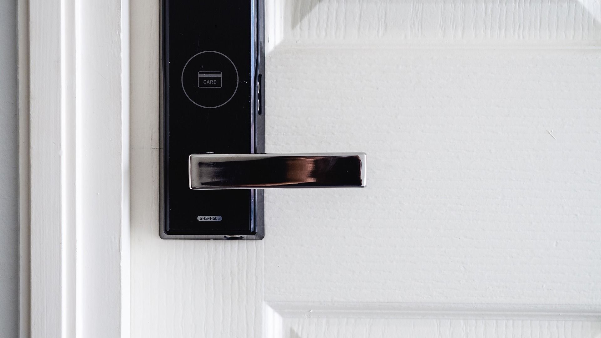 Black smart lock and silver door handle on white door.