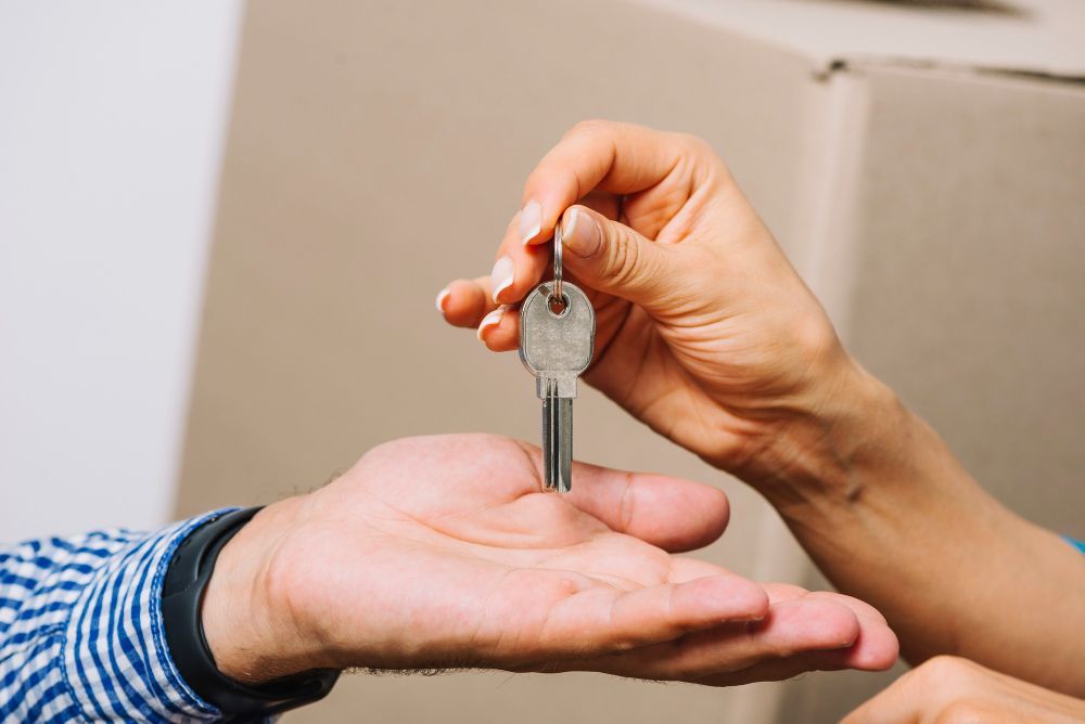 Person's hand giving house key to another person, likely a new homeowner.
