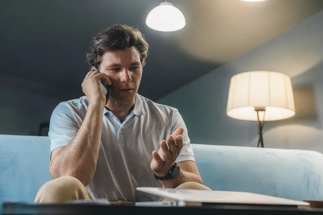 A man is sitting on a couch talking on a cell phone.