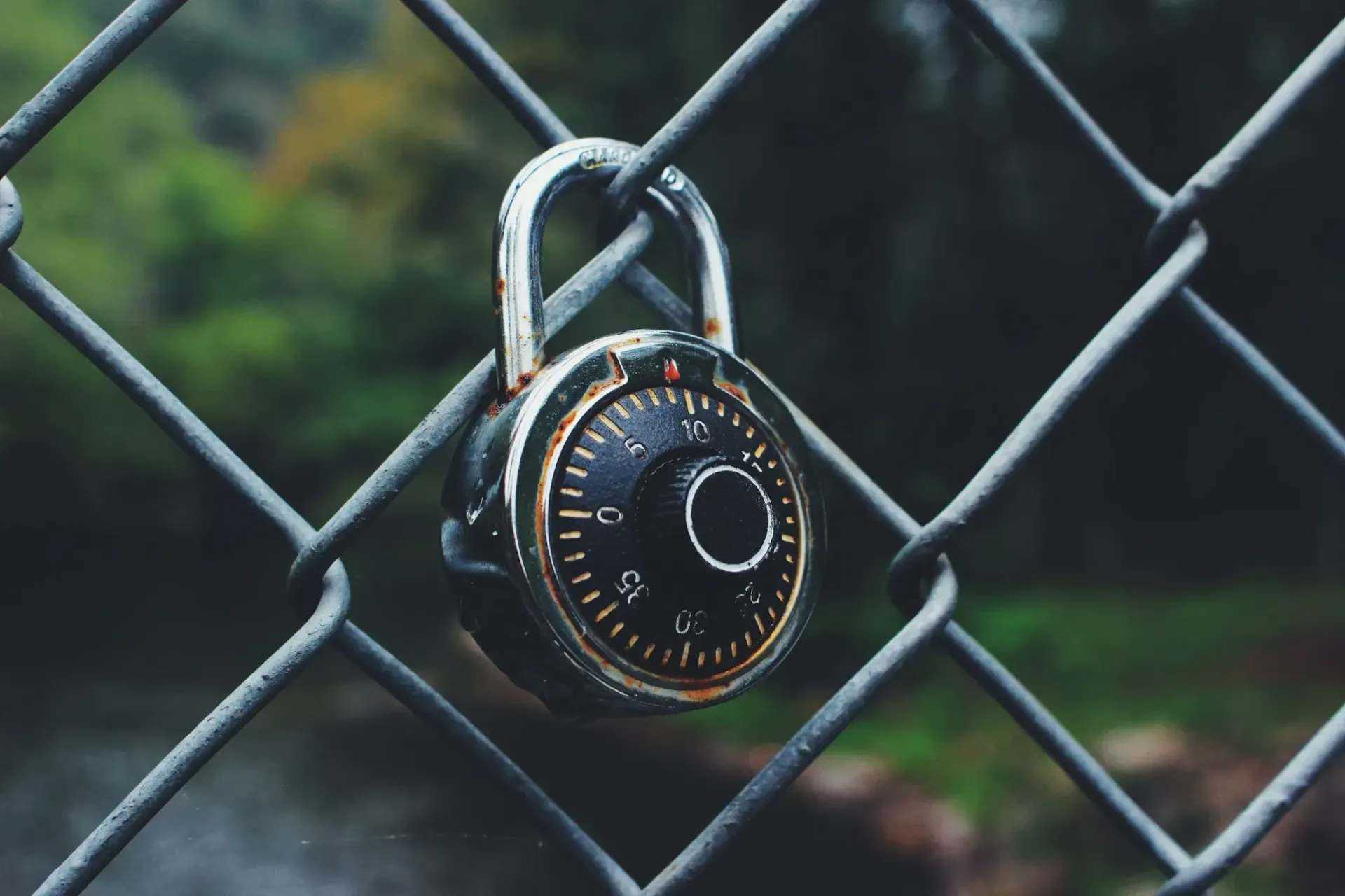 A close up of a padlock on a chain link fence.