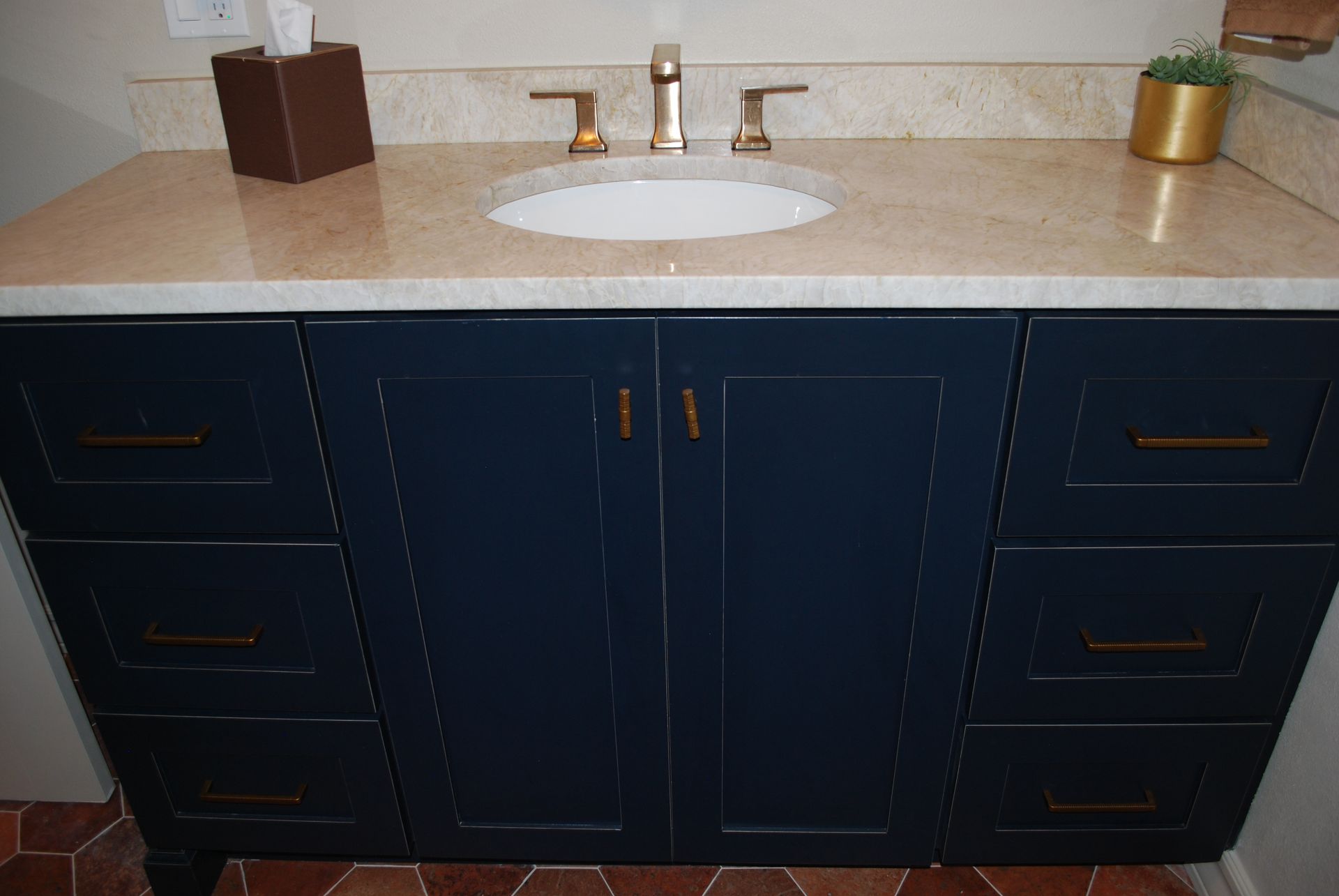 Navy blue bathroom vanity with gold hardware, tan countertop, and white sink.