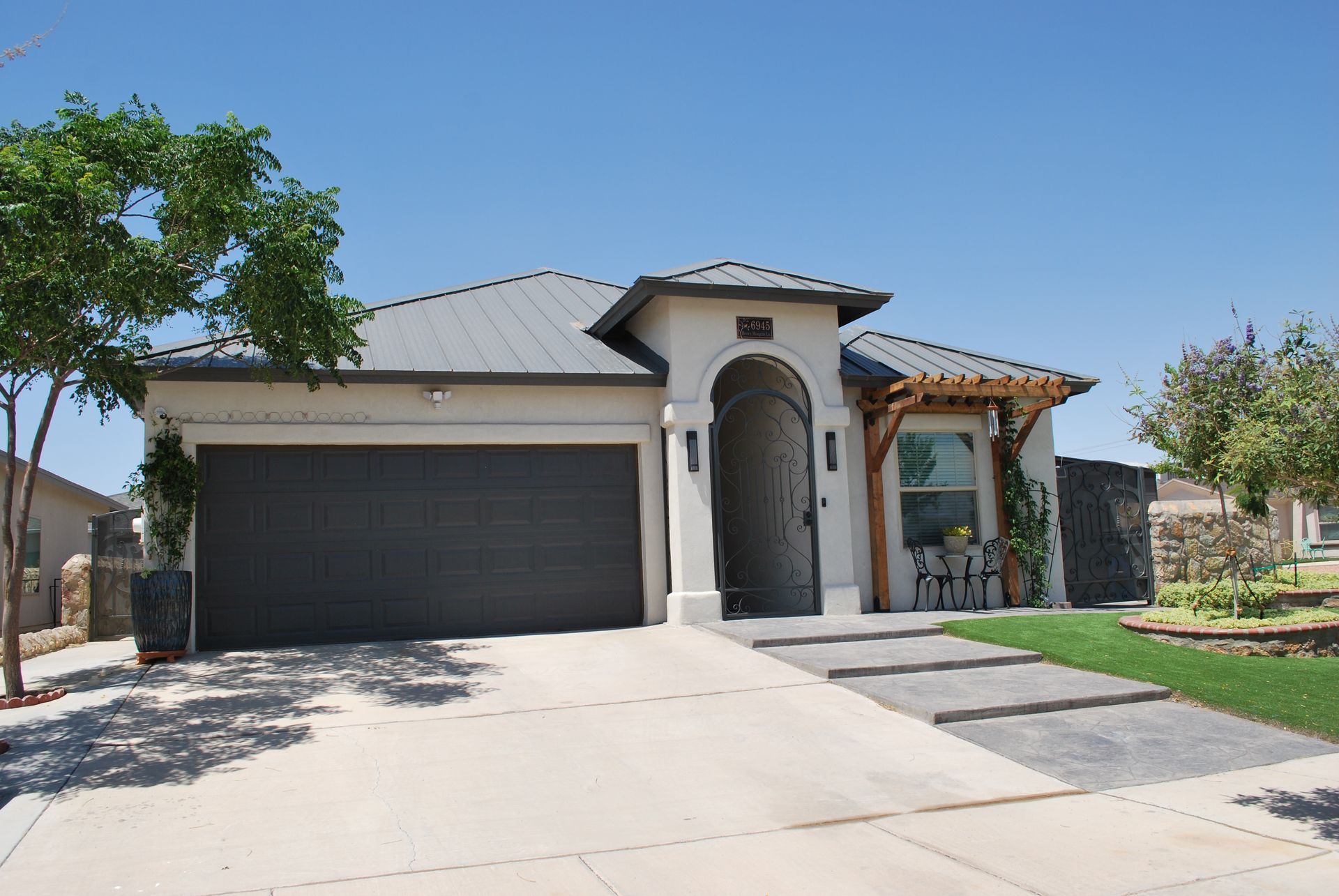 Tan house with gray roof, garage door, and walkway; blue sky.