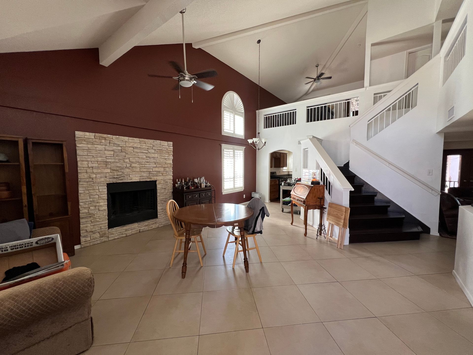 Spacious living room with a fireplace, dining area, and stairs leading to a second floor, featuring high ceilings and large windows.
