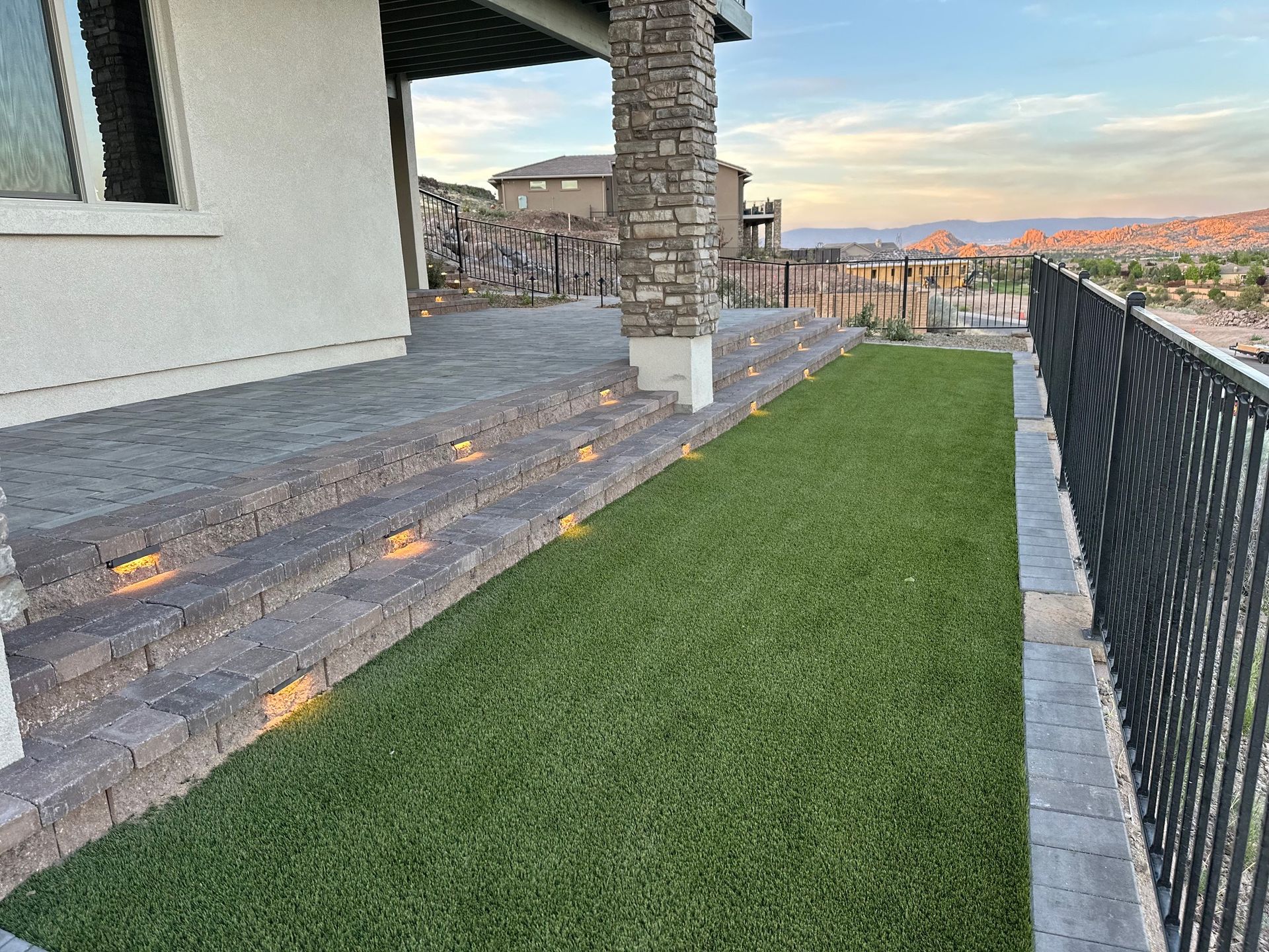 Front yard with green lawn, stone patio steps, black railing, and a house porch at sunset