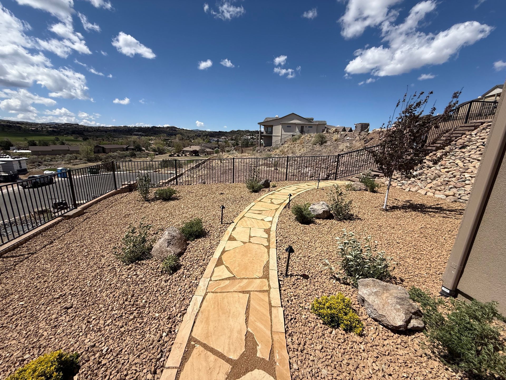 Flagstone path through a xeriscaped yard, leading towards a distant house under a blue sky.