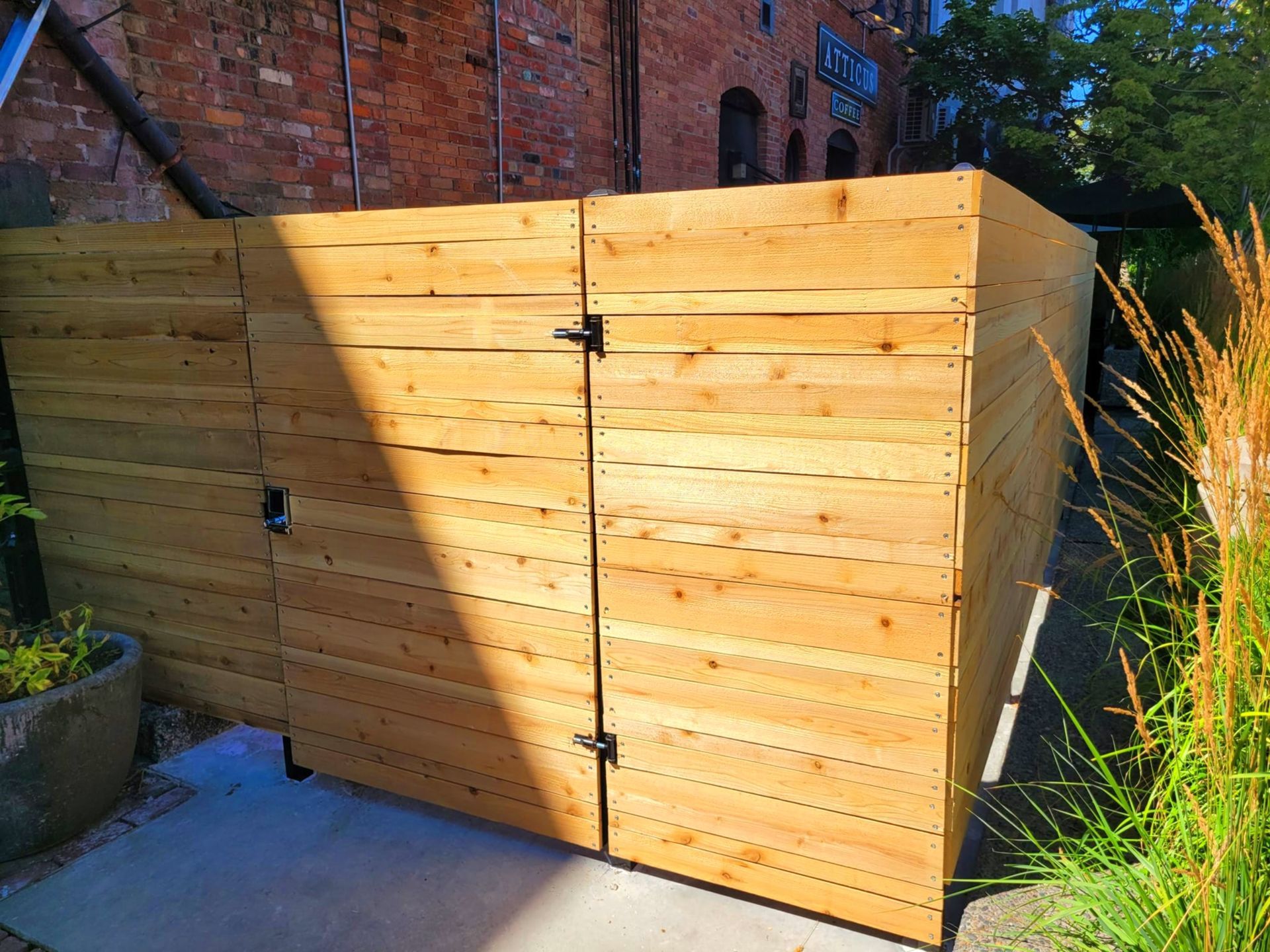 Wooden fence with closed double doors. Brick wall in background, sunlight.