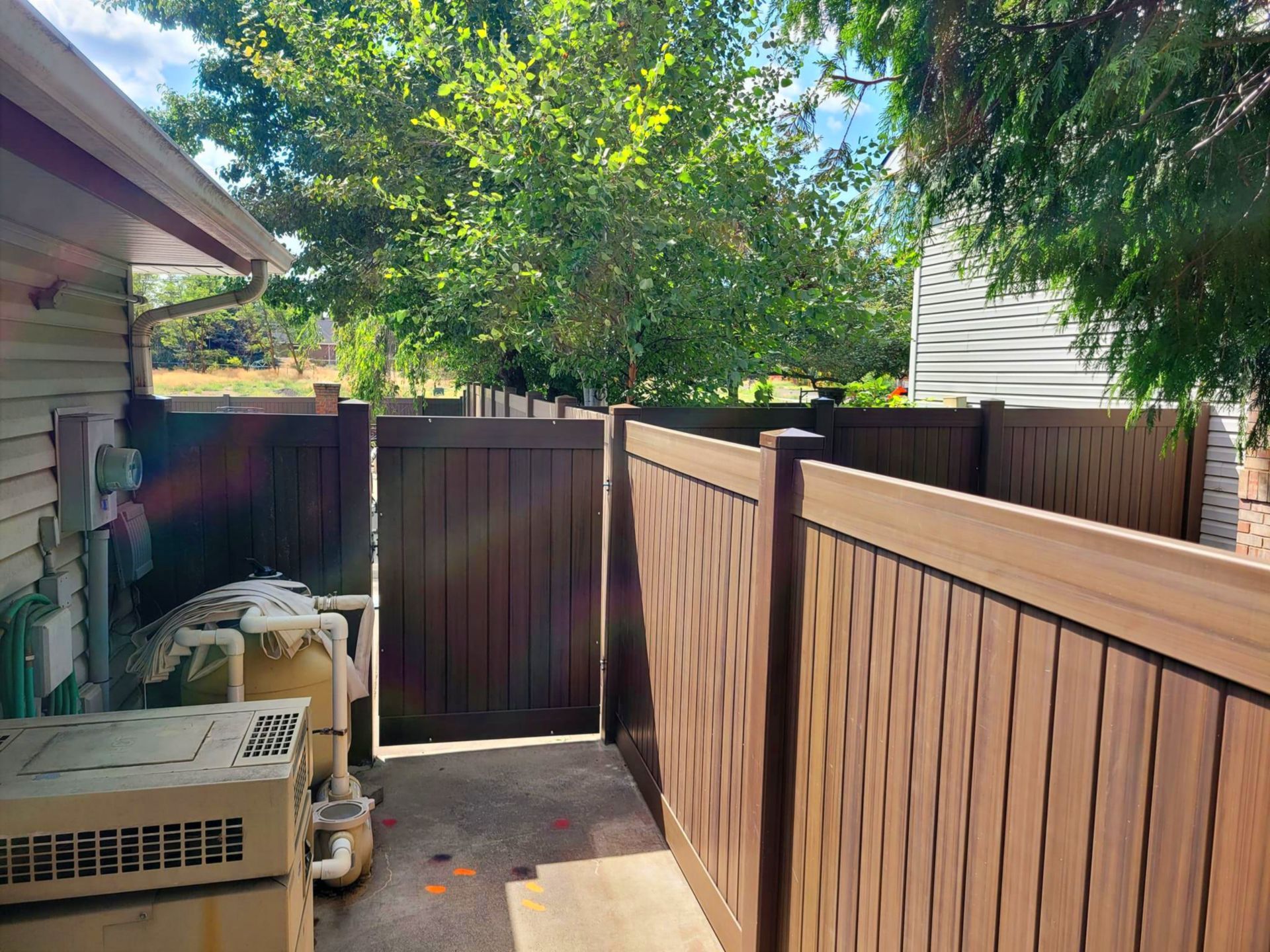 Brown privacy fence with gate surrounding a small patio near a house with an air conditioning unit.