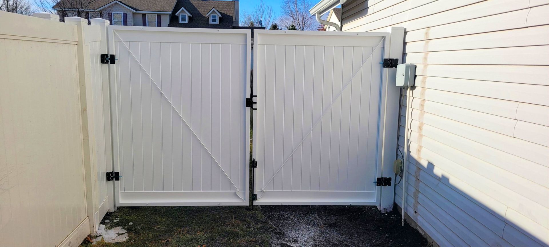 White vinyl double gate with black hardware, in front of a house.