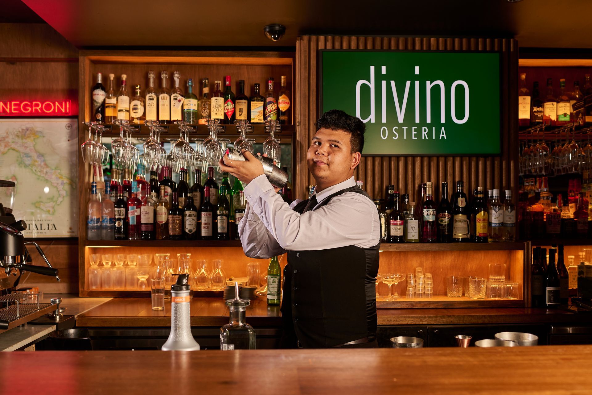 Bartender smiles while shaking a cocktail shaker behind a bar.