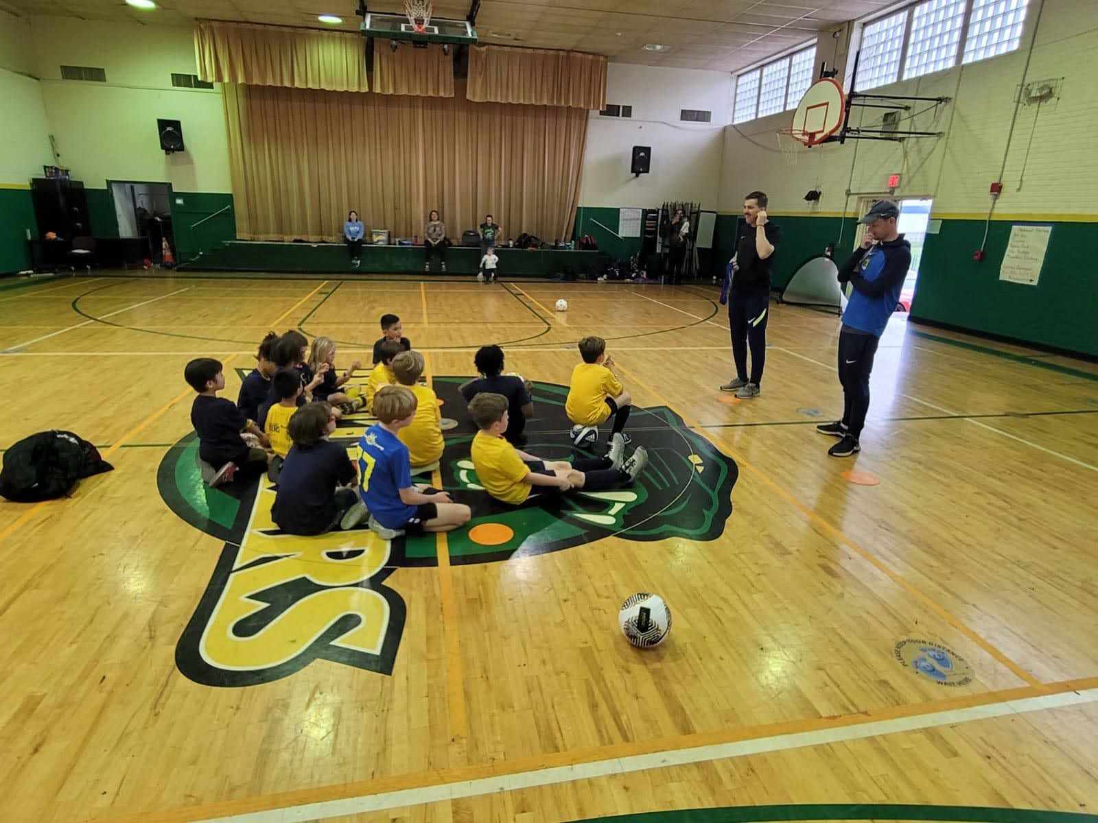 Olé FC children sitting while coaches talk to them