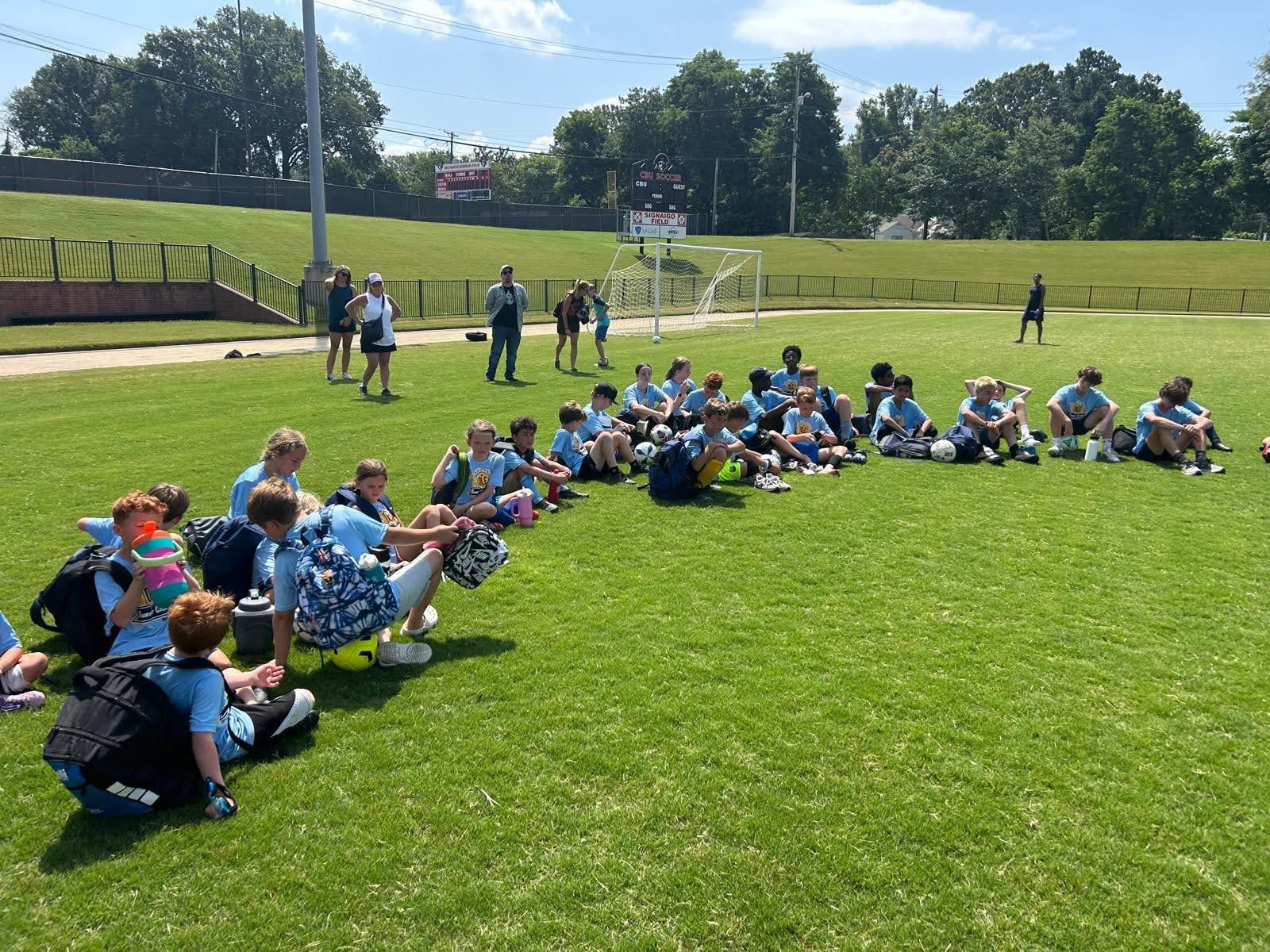 Olé FC children in blue jerseys sitting on a soccer field