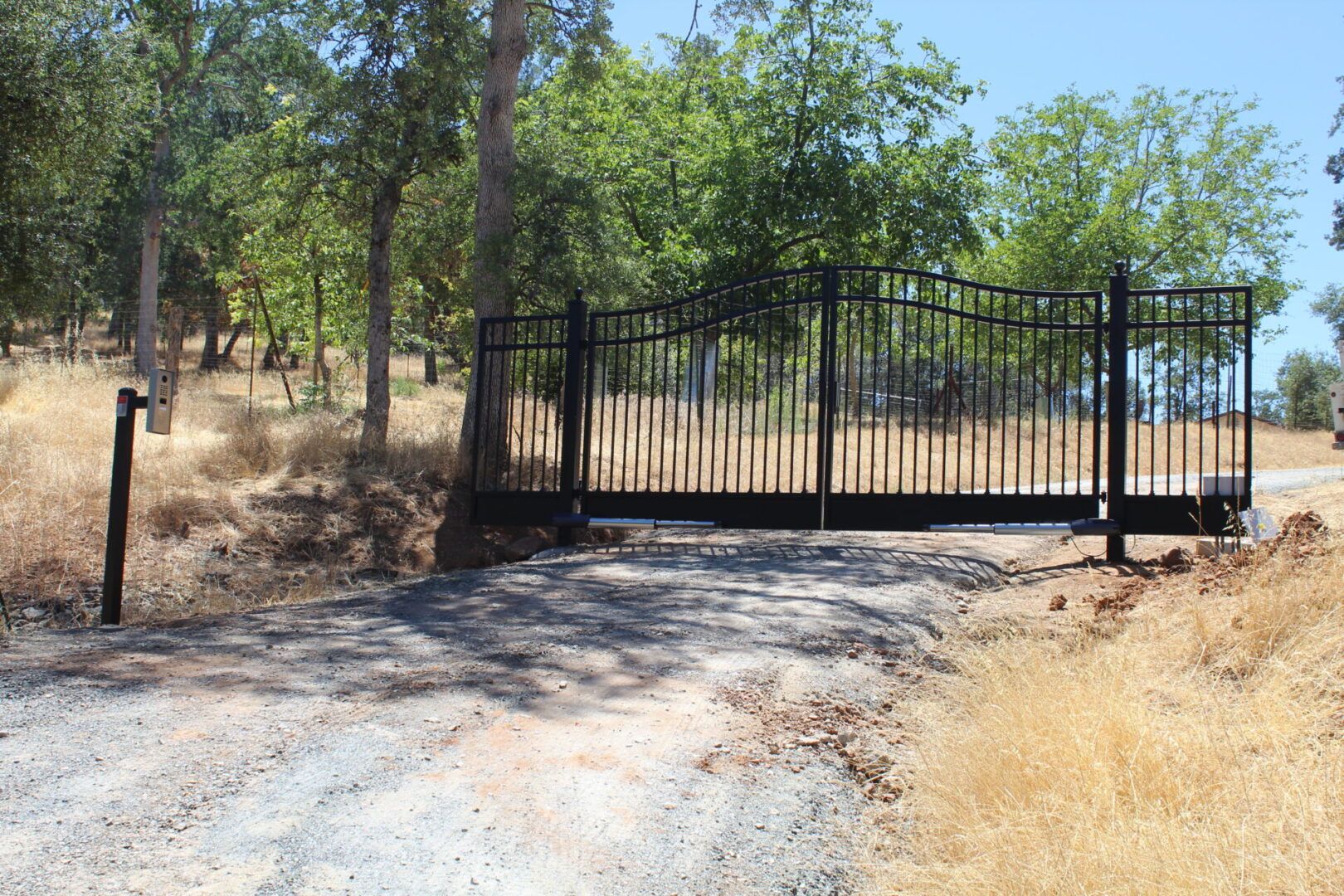 A black gate is sitting on the side of a dirt road.