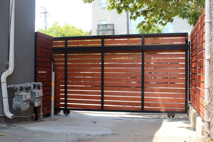 A wooden gate with horizontal slats and a black frame in an urban setting.