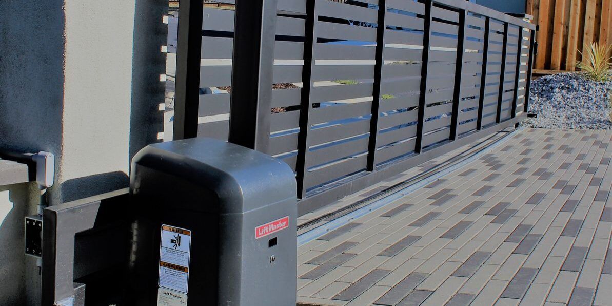 A sliding gate with a motor attached to it is sitting on a brick sidewalk.