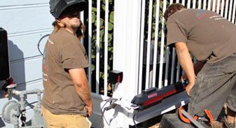 Two men wearing welding helmets are working on a fence.
