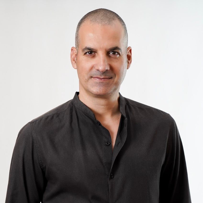 Man with shaved head, wearing a black shirt, looking at the camera.