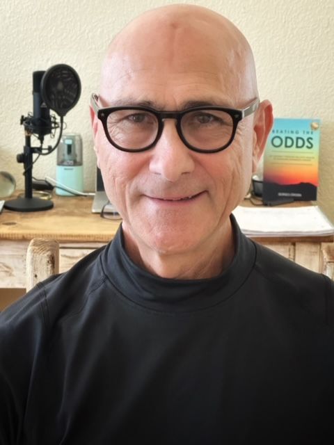 Bald man wearing glasses, black shirt, facing forward. Microphone, book 