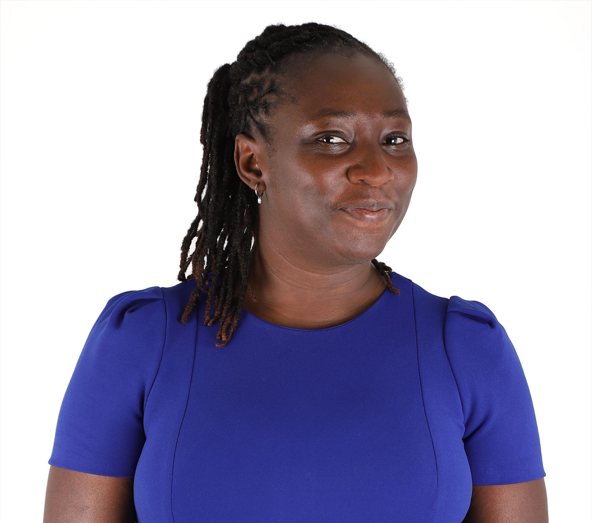 Woman with dreadlocks, wearing a blue dress, smiling slightly, against a white background.