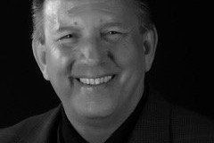 Man with a smiling expression, wearing a dark suit jacket, black and white portrait.