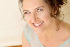 Woman smiling, blue-eyed with brown hair pulled back, wearing a light blue top.