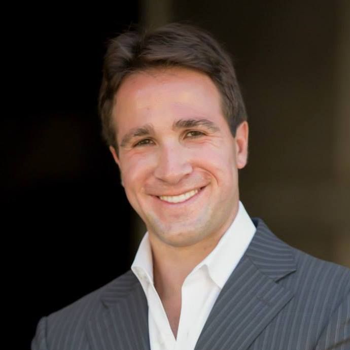 Man in suit jacket smiles, looking at camera.