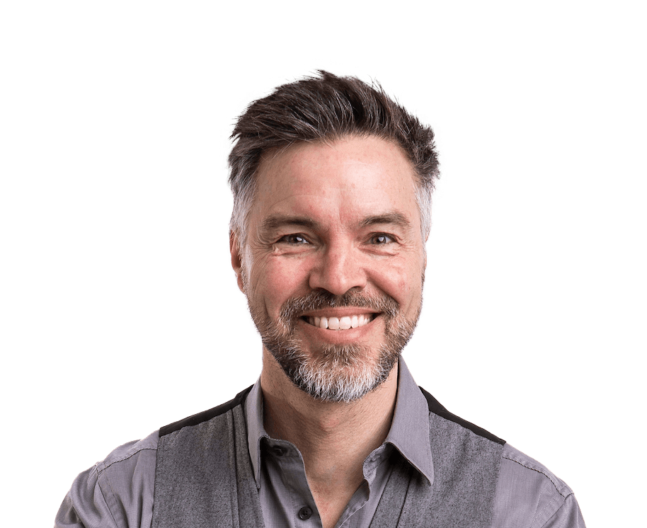 Man with graying hair and beard smiling, wearing a gray vest and collared shirt.