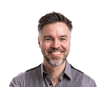 Man with graying hair and beard smiling, wearing a gray vest and collared shirt.