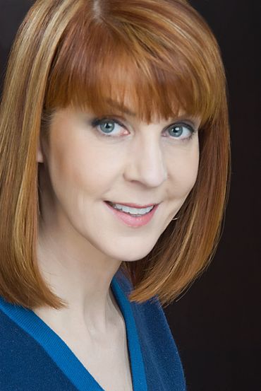 Woman with red hair and blue eyes, smiling, wearing a blue top.