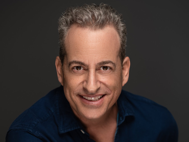 Man smiling, gray hair, navy blue shirt, dark gray background.