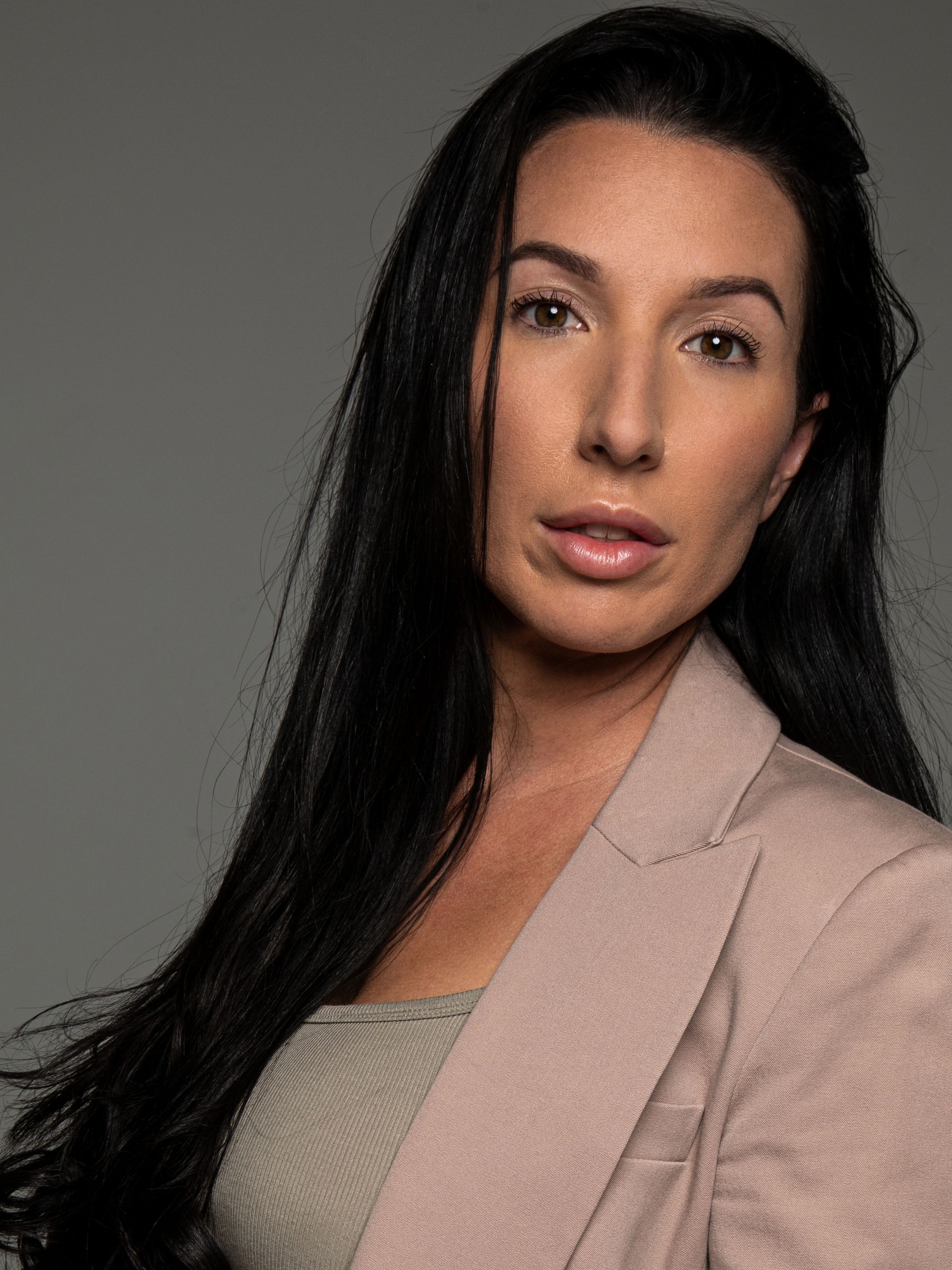 Woman in a pink blazer and gray top, with long dark hair, looking at the camera.