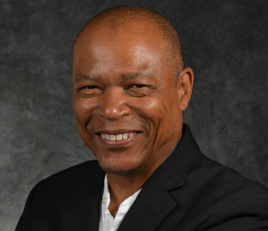 Smiling man in a black jacket and white shirt, against a dark grey background.