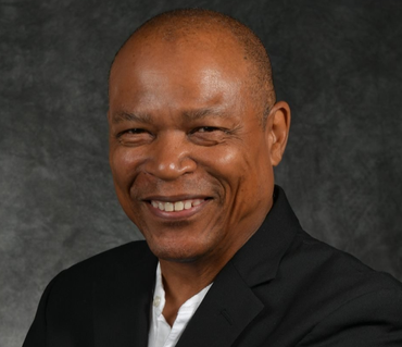 Smiling man in a black jacket and white shirt, against a dark grey background.