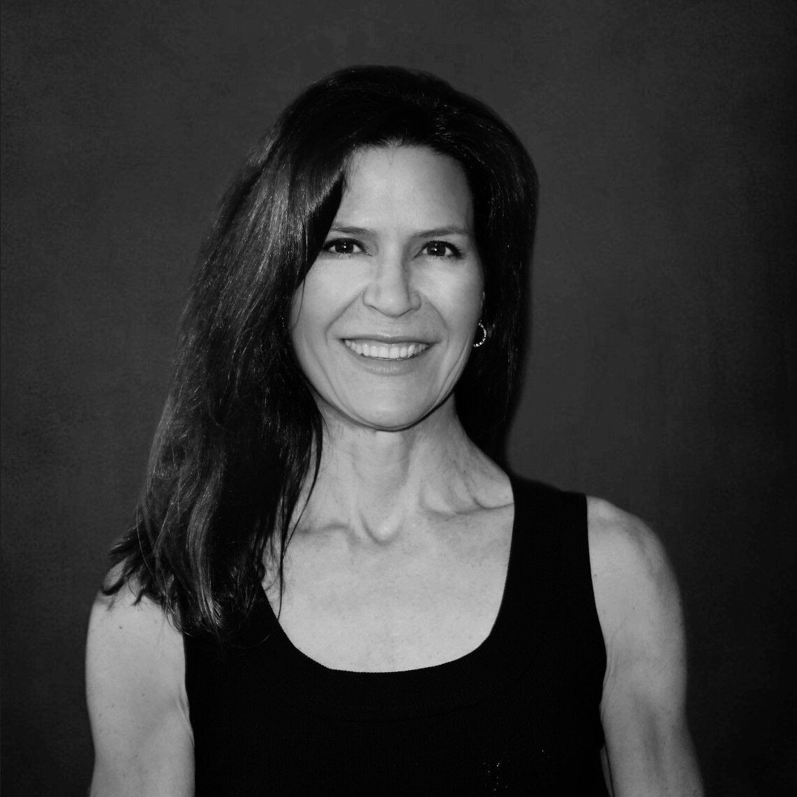 Woman smiling, dark hair, sleeveless black top, against a dark background.