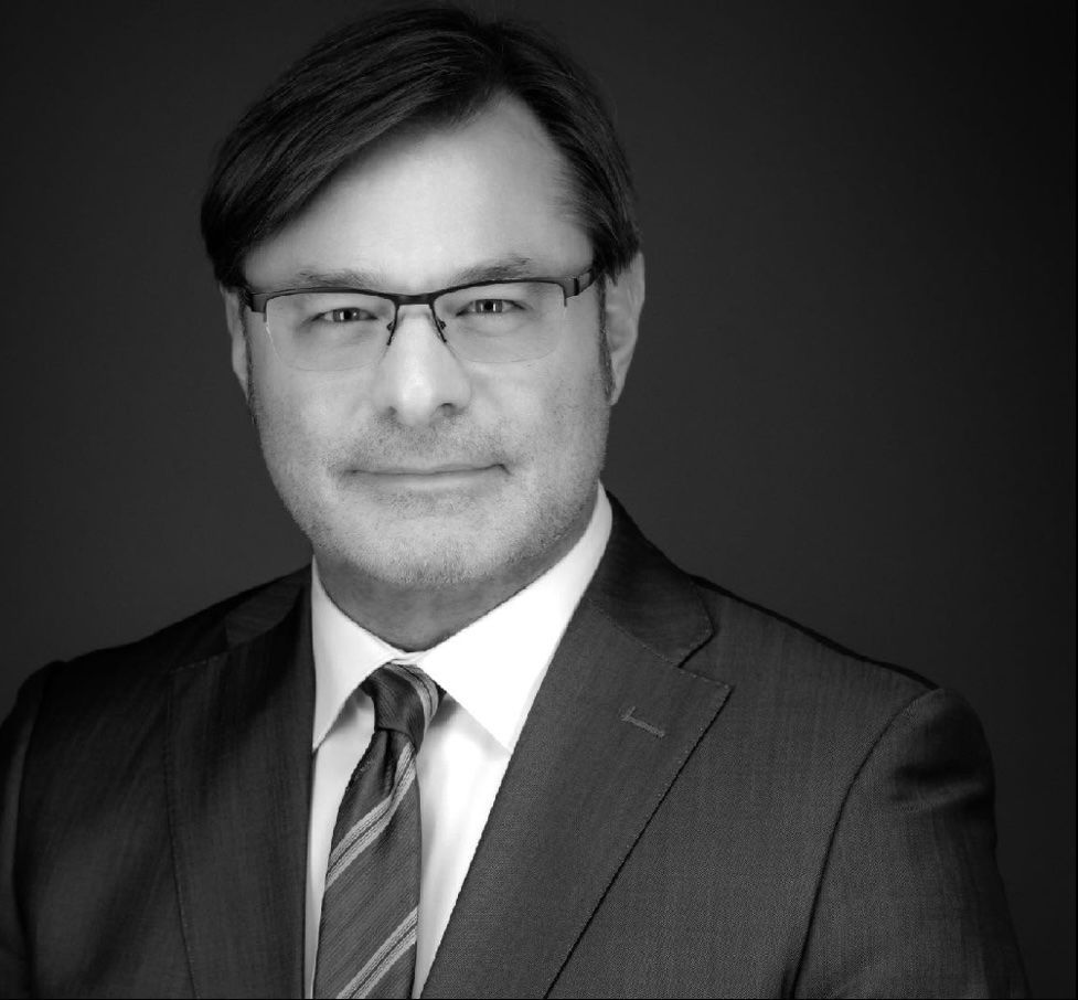 Man in suit and glasses looking at the camera, professional headshot.
