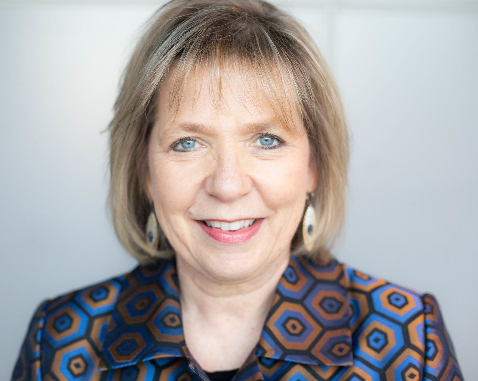 Woman smiling in a blue and brown patterned blazer, white background.