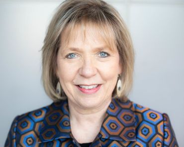 Woman smiling in a blue and brown patterned blazer, white background.