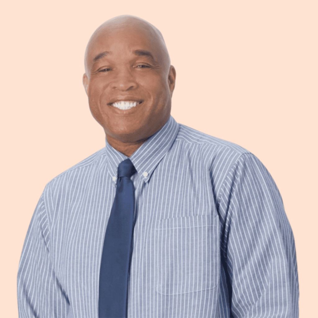 Man with a bald head smiles, wearing a blue striped shirt and tie, on an orange background.