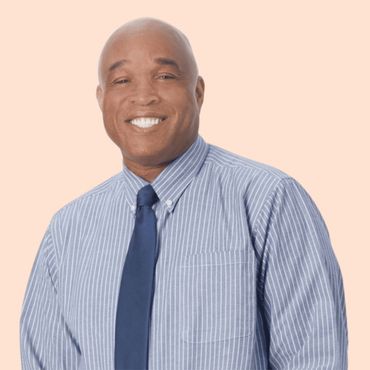 Man with a bald head smiles, wearing a blue striped shirt and tie, on an orange background.